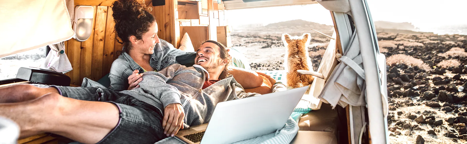 Happy young couple relaxing in their campervan with their dog at the beach.