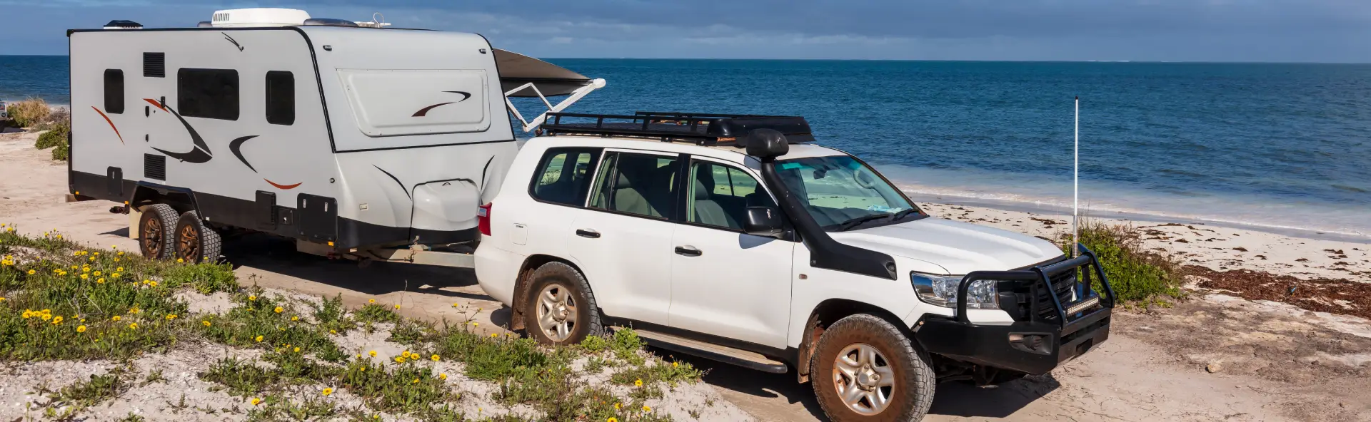Four wheel drive towing caravan on white sandy beach