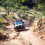 An older 4WD vehicle driving over uneven Australian terrain.