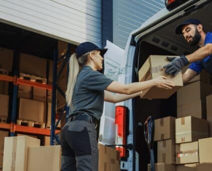 Two delivery workers unloading boxes from a commercial van outside a warehouse, representing small business operations supported by vehicle financing.