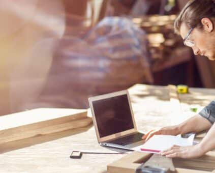 Man reviews plans at workshop bench with laptop and tools. Links to low doc car loans and a simple path for business finance.