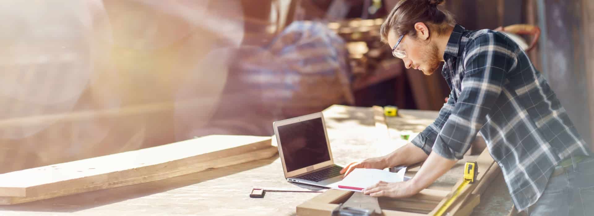 Man reviews plans at workshop bench with laptop and tools. Links to low doc car loans and a simple path for business finance.
