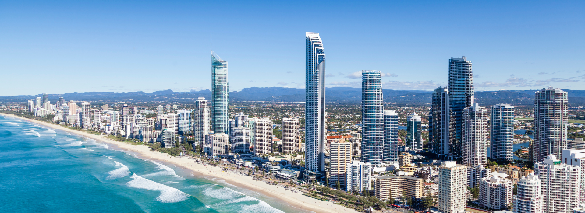 A panoramic view of Surfers Paradise on Queensland’s Gold Coast, showcasing the iconic Q1 Resort & Spa towering above surrounding beachfront skyscrapers, with turquoise waves rolling onto the white sand beach.