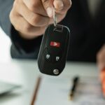 Hand holding car keys with toy car and laptop in background, representing successful car loan pre-approval process