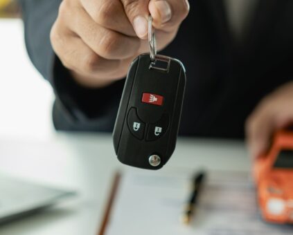 Hand holding car keys with toy car and laptop in background, representing successful car loan pre-approval process