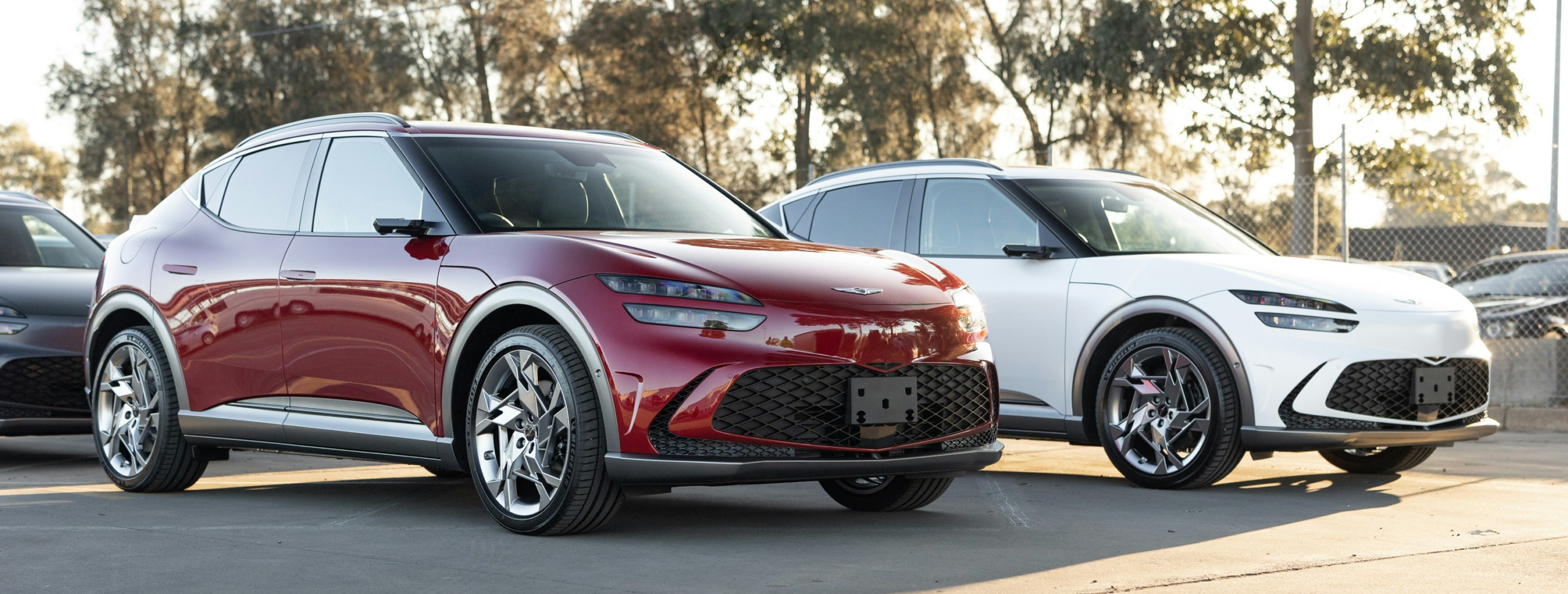 Two Genesis GV60 electric SUVs in red and white parked at an Australian dealership, representing EV finance options available through Fox Finance Group.
