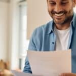 Australian at a kitchen table reviewing loan statements on a laptop, relaxed