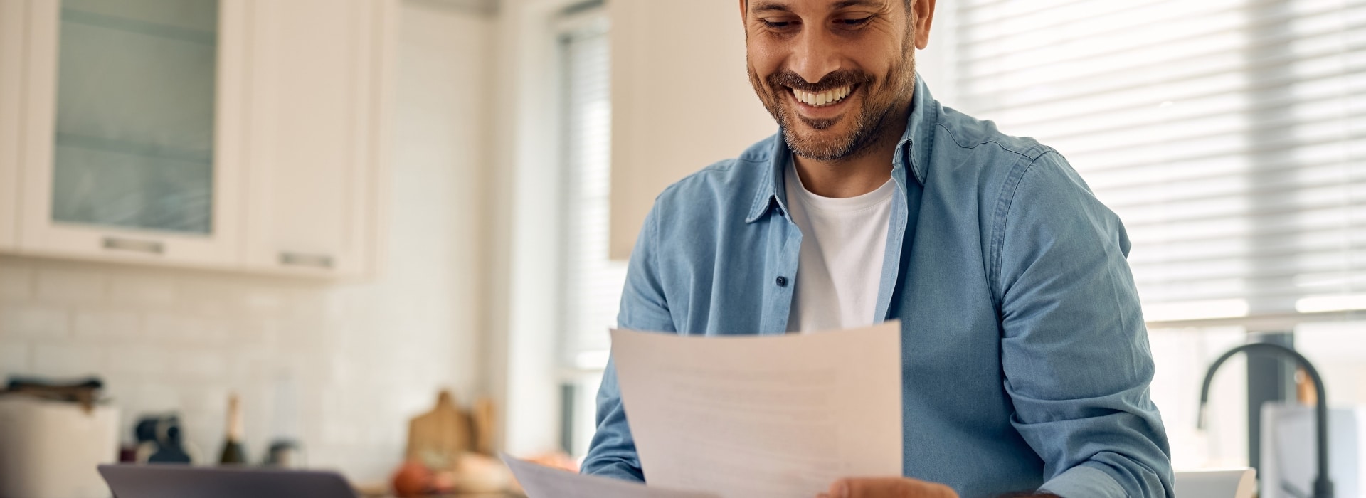 Australian at a kitchen table reviewing loan statements on a laptop, relaxed