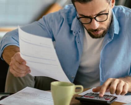 A person sitting at a kitchen table with a car loan statement and a phone, working out whether to refinance.