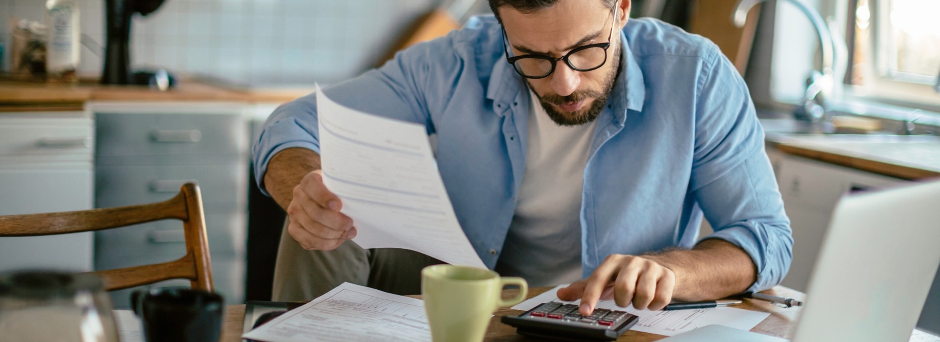 A person sitting at a kitchen table with a car loan statement and a phone, working out whether to refinance.